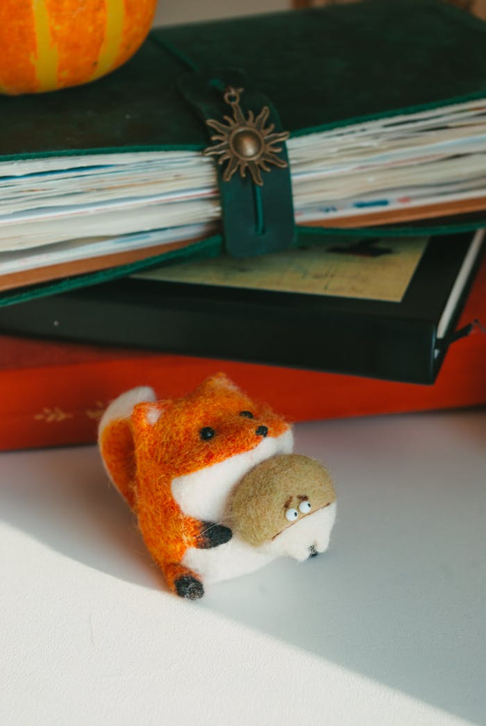 Cute felt fox toy on a desk with a stack of books in natural light.
